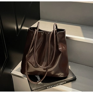 Detailed view of the glossy dark brown tote bag placed on a magazine on steps