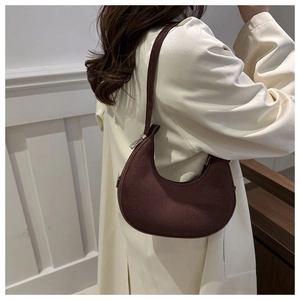 Detail of dark brown suede crescent hobo bag with adjustable strap on beige coat