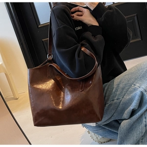 Detail of large dark brown patent leather tote bag shown on model for daily commuting