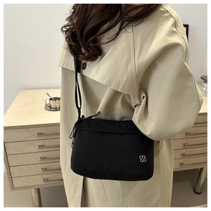 Detail of a minimalist black nylon crossbody bag featuring a silver floral metal accent