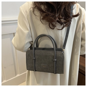 Model wearing dark grey corduroy handbag with cream blazer in an elegant room setting