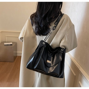 Détail du sac cabas en cuir noir avec poche à fermoir doré et bandoulière en chaîne métal