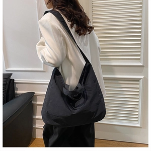 Minimalist large black tote bag with wide strap worn by model in chic interior
