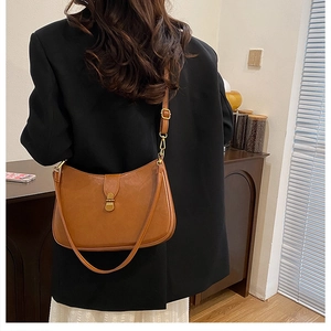 Detail of adjustable strap and gold hardware on a brown leather crescent shoulder bag