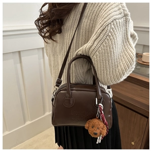 Detail of dark brown leather Boston bag with plush teddy charm and adjustable strap