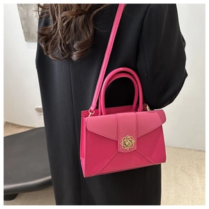 Detail of flamingo pink envelope bag with gold floral lock worn on a black blazer