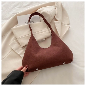 Detail of dark brown suede hobo bag with silver rivets placed on a white blazer