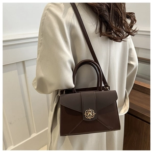 Detail of dark brown leather crossbody bag with golden geometric floral metal buckle