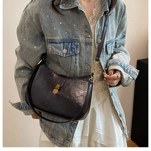 Close-up of black crescent bag with lychee texture and gold buckle on denim jacket