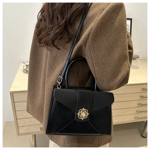 Close-up of black retro square bag with golden flower metal clasp on brown wool blazer