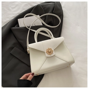 Close-up of white leather envelope handbag with a gold petal-shaped metal clasp detail
