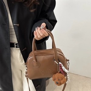 Brown leather handbag with teddy bear charm and shoulder strap shown in a casual lifestyle pose