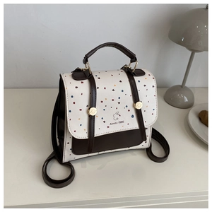 Detail of cream backpack with colorful speckles and brown leather straps on a table