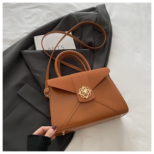 Detail of a brown leather envelope bag featuring a gold floral buckle and protective feet