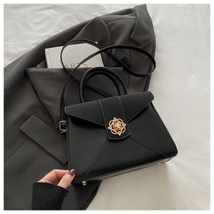 Close-up of black crossbody bag featuring gold clover clasp and matte leather texture