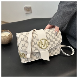 Detailed macro view of the cream monogram pattern and gold metal M logo on the shoulder bag