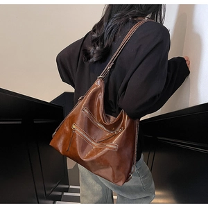 Détail du grand sac cabas marron foncé brillant avec fermetures éclair porté par un mannequin