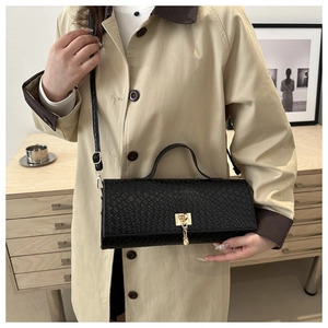 Close-up of black snake-textured crossbody bag with golden buckle on a beige coat