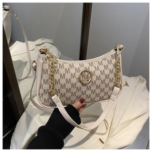 Detail of beige crescent underarm bag featuring repetitive M patterns and gold logo chain