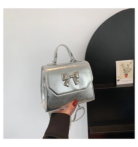 Détail du sac argenté effet miroir avec nœud 3D et fine bandoulière élégante