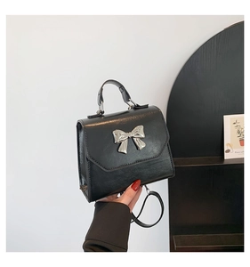 Détail d'un sac à bandoulière noir brillant avec boucle noeud argentée et poignée ronde