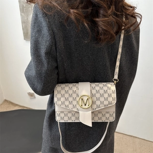 Minimalist beige underarm bag with monogram print and golden M buckle shown on shoulder