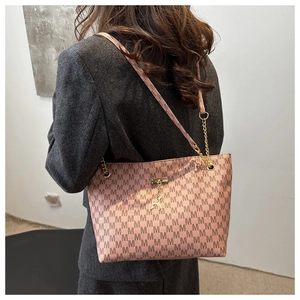 Detail of coral pink tote bag with brown M-pattern and gold deer pendant on chain strap
