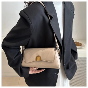 Close-up of minimalist beige crossbody bag with adjustable strap on a black blazer model