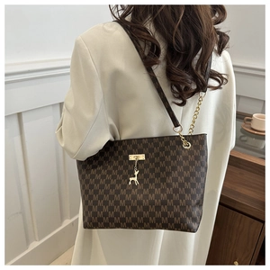 Detail of brown tote bag with M monogram pattern and golden deer pendant on shoulder
