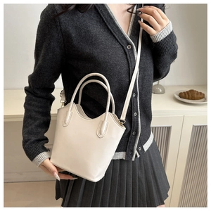 Detail of a chic cream leather bucket bag with cylindrical handles and a thin shoulder strap