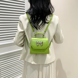 Mini sac à dos vert clair avec nœud argenté porté par un mannequin en tailleur beige