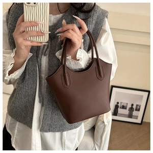 Close-up of minimalist dark brown bucket bag with curved edges and dual handles