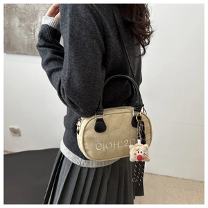 Detail der beigen strukturierten Handtasche mit weißer Stickerei und Plüschbär-Anhänger