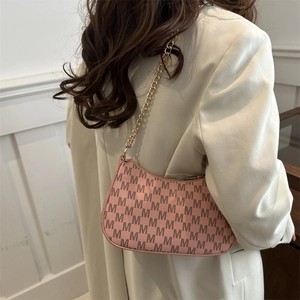 Pink crescent hobo bag with M-pattern and gold chain strap shown on model's shoulder