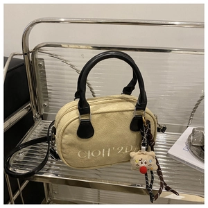 Detailansicht der beigen Wildleder-Bowlingtasche mit schwarzen Griffen und Bärenanhänger