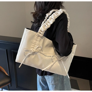 Detail of cream tote bag featuring ruched cloud-style straps and decorative bows