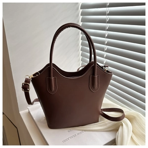 Brown bucket bag on books featuring wavy top design and golden metal buckle details