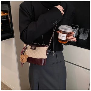 Détail du sac seau bandoulière avec surpiqûres matelassées, cuir verni et breloque ours