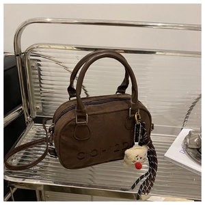 Nahaufnahme der braunen Plüschhandtasche mit Logo-Prägung und niedlichem Bären-Anhänger