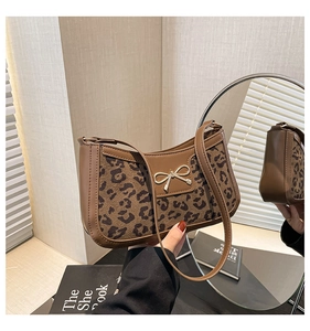 Detail of a brown leopard print crescent bag featuring a golden metal bow ornament
