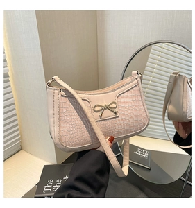 Close-up of light pink crocodile pattern crescent bag with metal bow detail