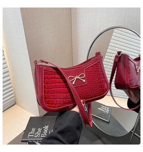 Detail of red croc-embossed crescent bag with a decorative gold bow metallic accent