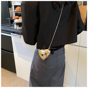 Détail d'un sac bandoulière doré en forme de cœur avec finition facettée et chaîne fine