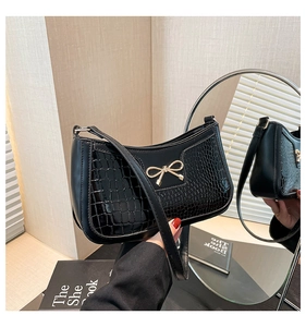 Close-up of black crescent bag with croc-embossed texture and golden bow detail