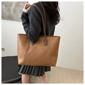 Detail of a brown tote bag with snake skin texture and slim handles worn on shoulder