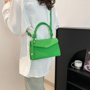 Bright green woven crossbody bag with knotted handle shown on model in white shirt