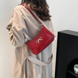 Red crescent shoulder bag with crocodile texture and golden bow worn with a beige coat