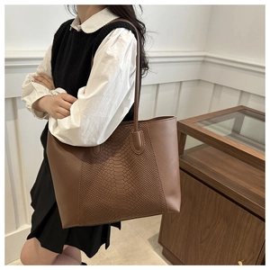 Brown tote bag with snakeskin texture detail on arm of model in minimalist setting