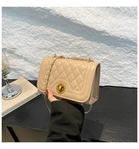 Detail of beige quilted shoulder bag featuring gold chain strap and metal twist lock