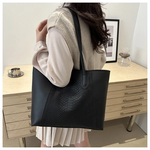 Detail of a large black tote bag featuring snakeskin texture and smooth leather panels